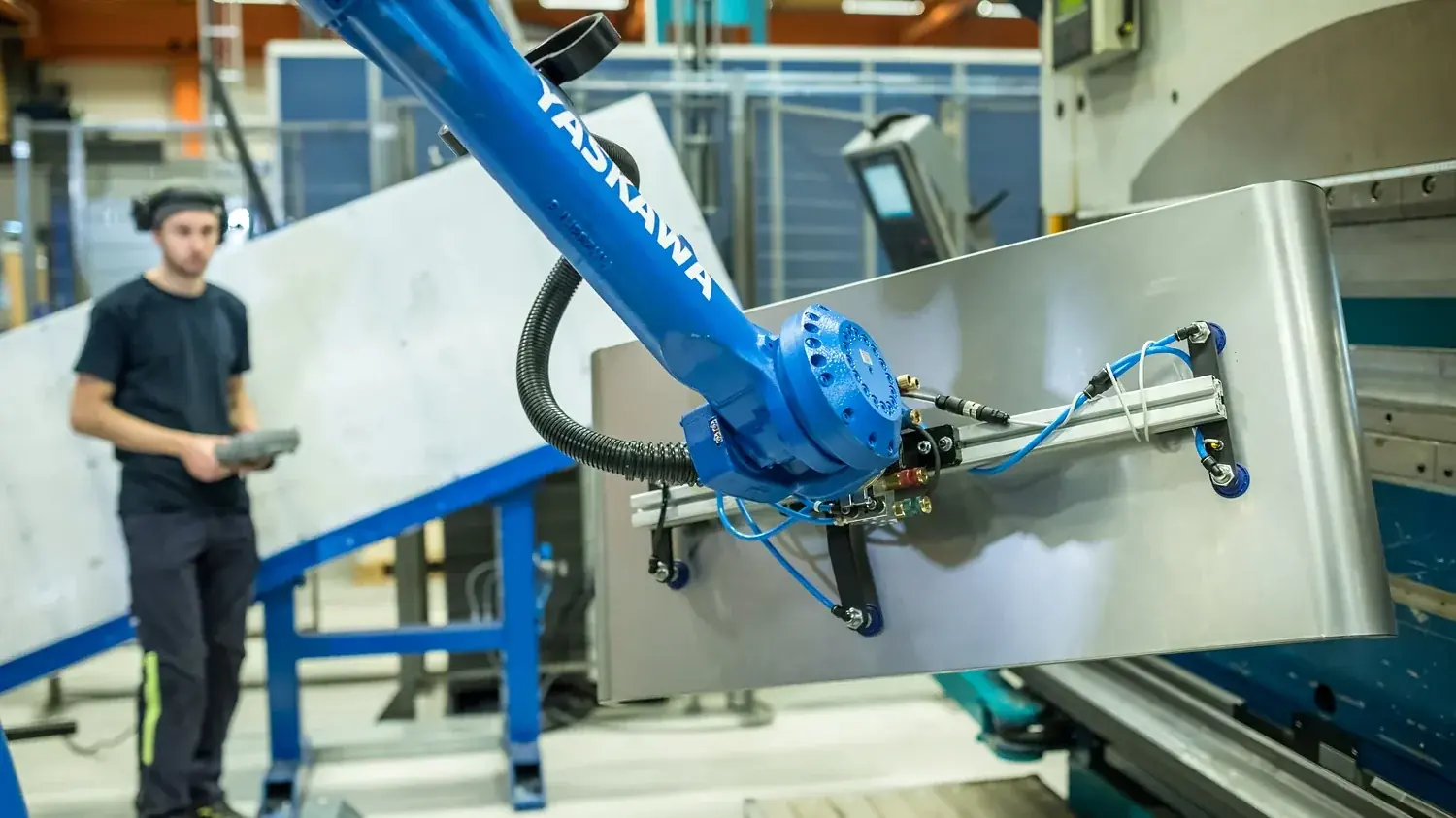 Operatör vid robotarm som hanterar en stor vit plåtpanel