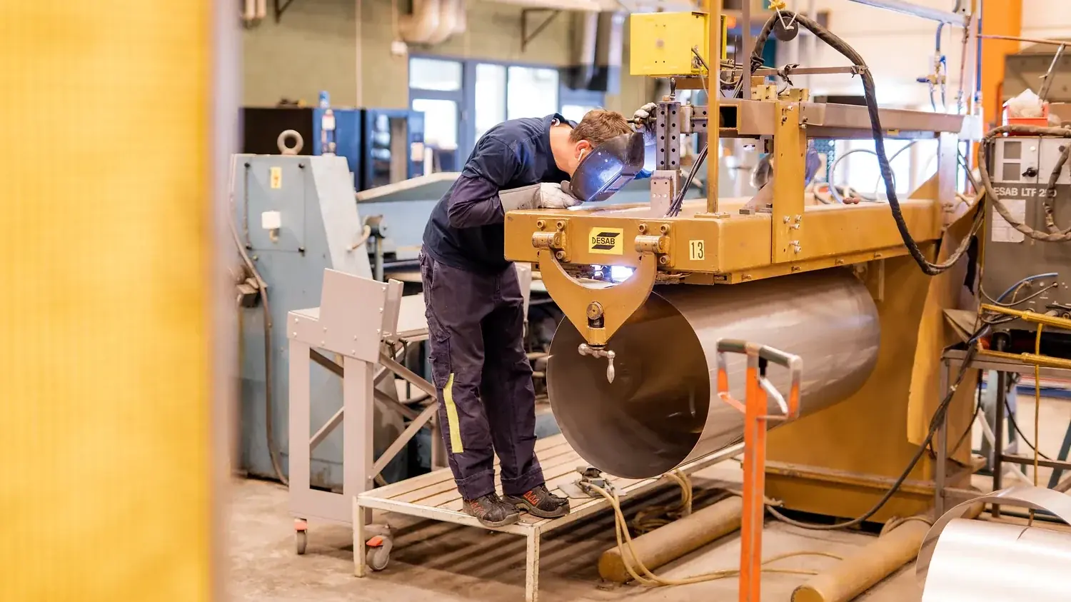 Medarbetare arbetar med en stor cylindrisk behållare i verkstaden