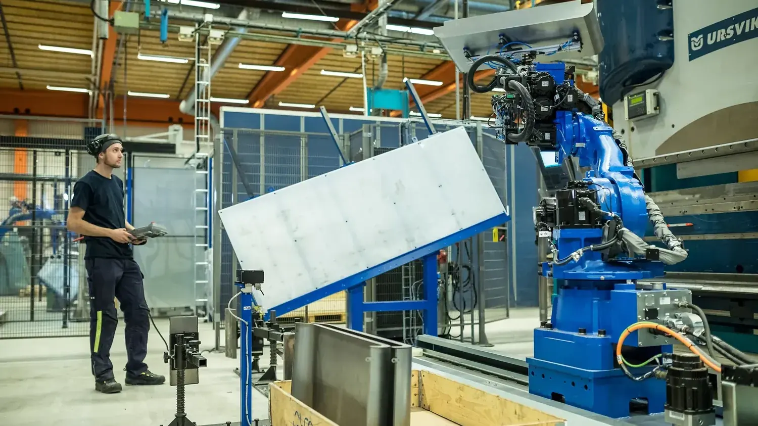 Operatör vid robotcell där en stor plåtpanel lyfts och vänds