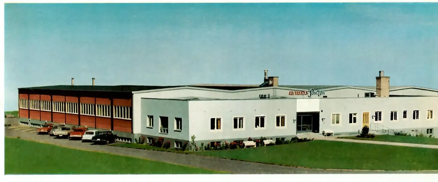 Historiskt foto av Tranås Rostfrias fabriksbyggnad med bilar parkerade utanför